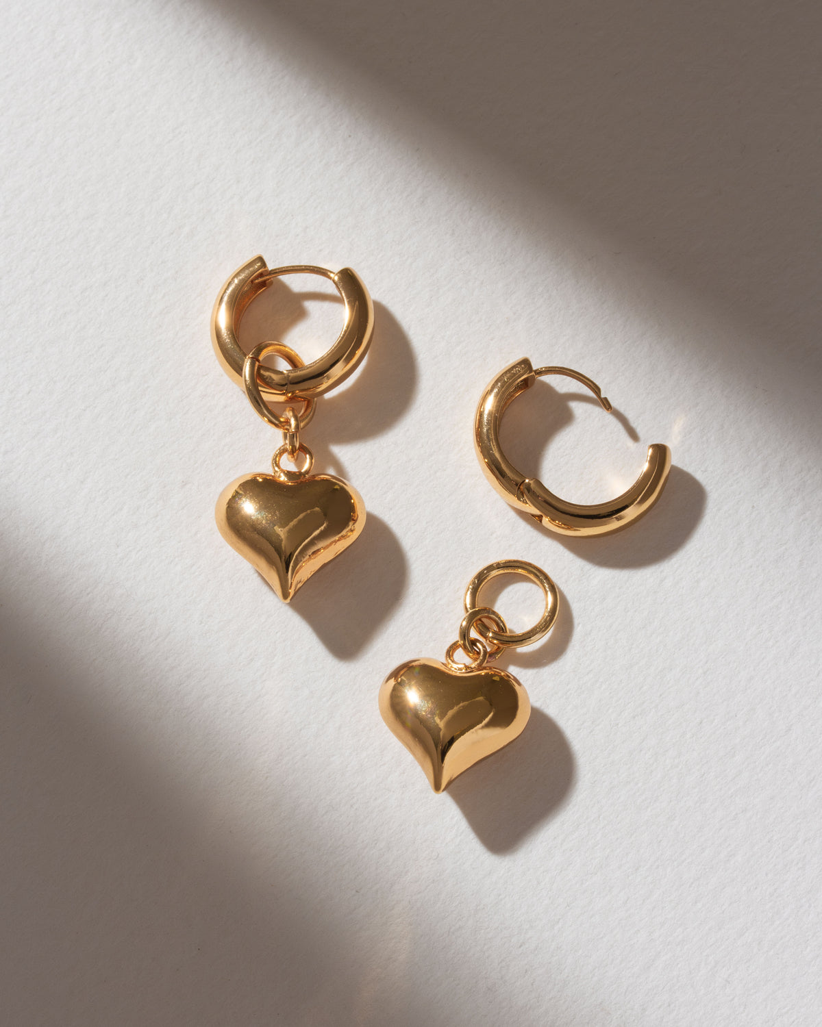 Gold Milano Amulet 2-in-1 charm huggie hoop earrings with heart charms shown on a white surface.