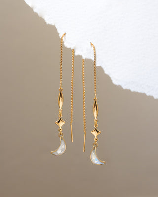 Gold earrings with moon-shaped charms on a textured beige background