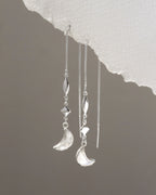 Silver earrings with moon and star designs on a textured gray background