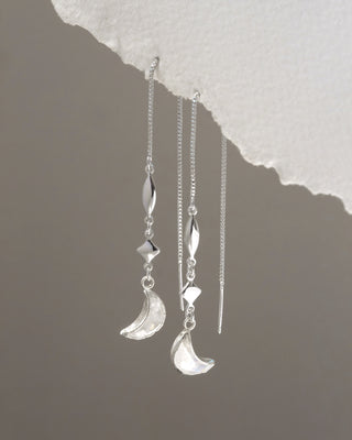 Silver earrings with moon and star designs on a textured gray background