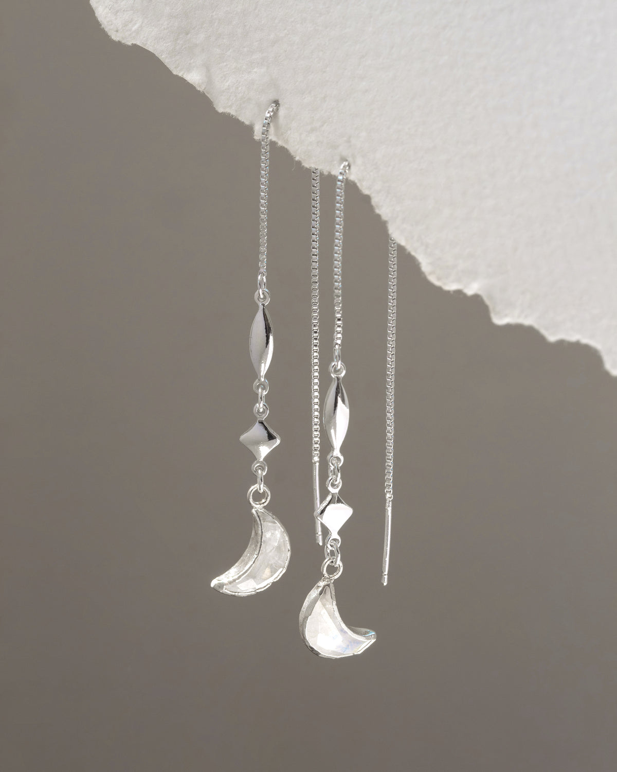 Silver earrings with moon and star designs on a textured gray background