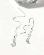 Silver threader earrings with star and moon charms are displayed on a white surface.