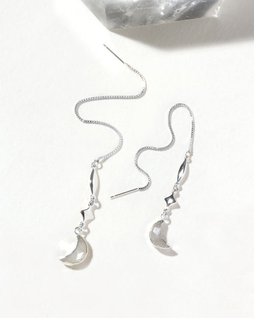 Silver threader earrings with star and moon charms are displayed on a white surface.