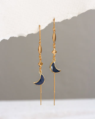 Gold earrings with blue crescent moon designs on a neutral background