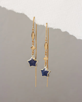 Gold earrings with star-shaped charms on a gray background