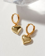 Pair of shiny gold Milano Amulet Huggie Hoop Earrings with heart charms.