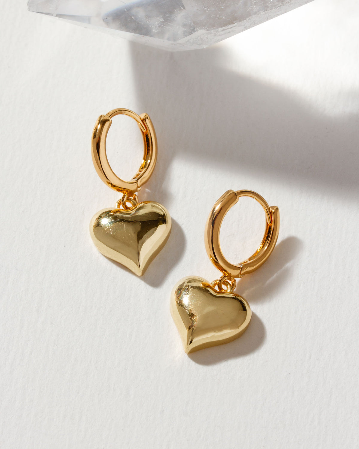 Pair of shiny gold Milano Amulet Huggie Hoop Earrings with heart charms.