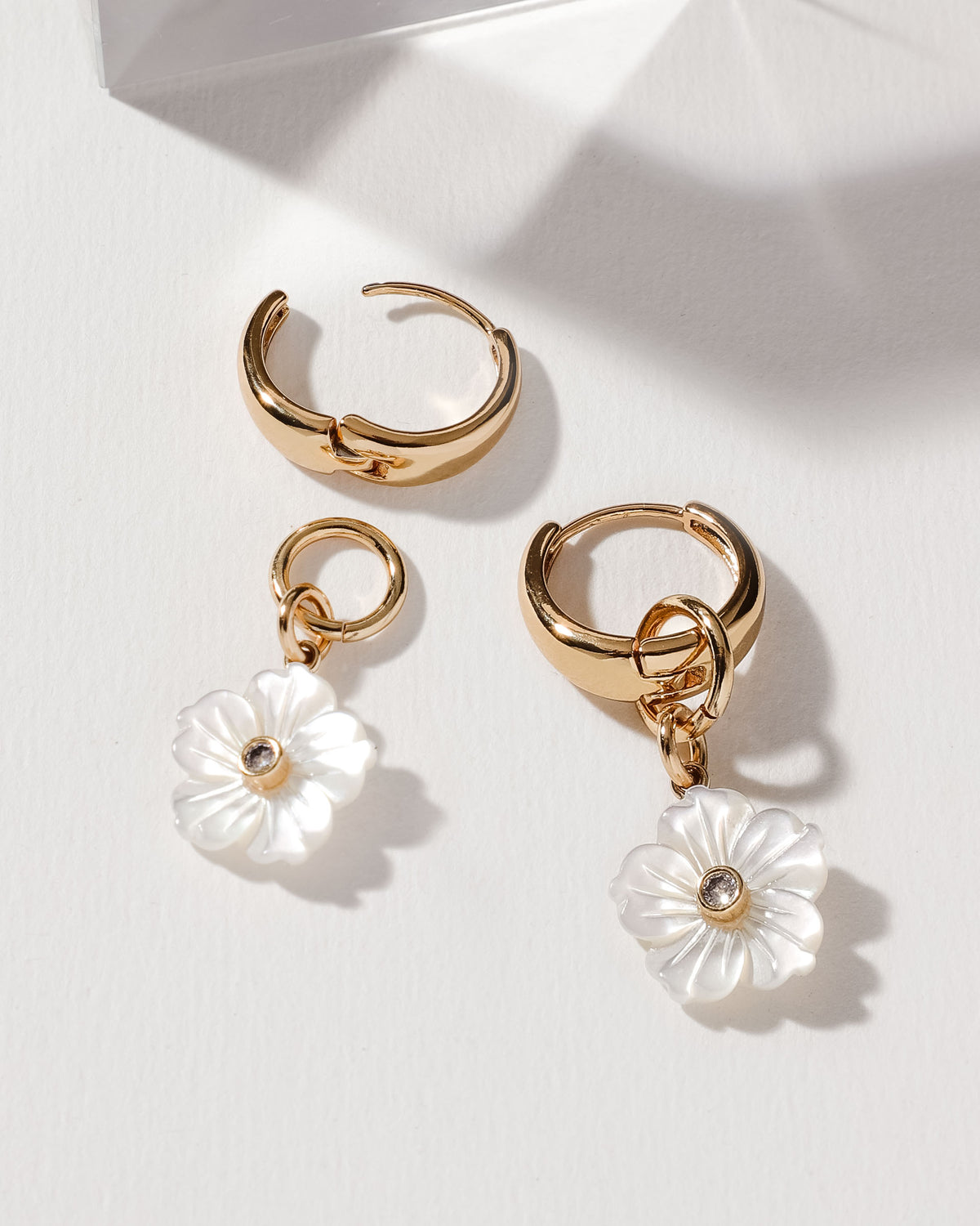 Gold huggie hoop earrings with a removable, carved mother of pearl flower charm and CZ center.