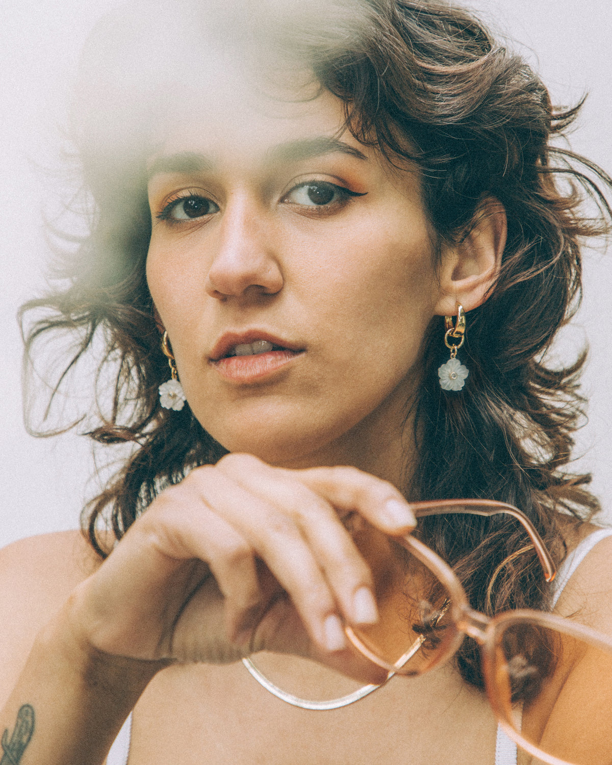 Model wearing gold Tulum Flora 2-in-1 Charm huggie hoops with white flower charm.