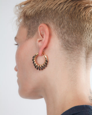 A close-up side profile of a person wearing a gold hoop earring adorned with dangling dark gun metal links.