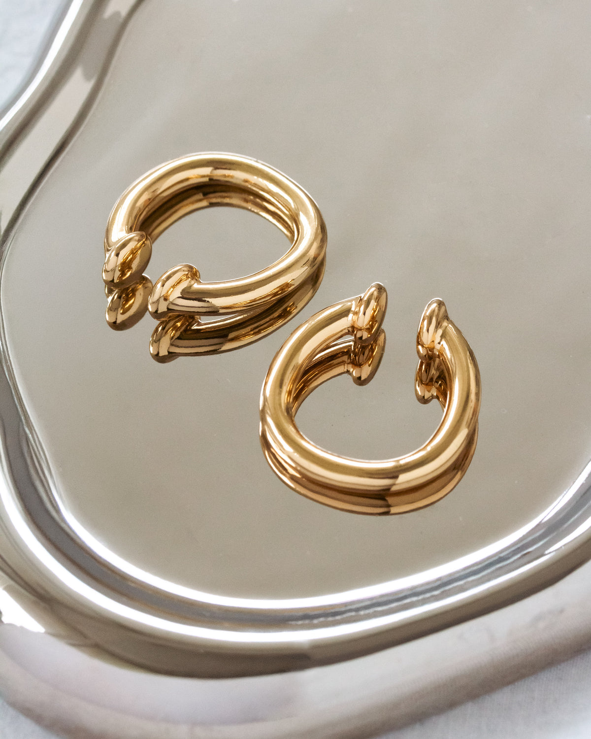 Gold hoop earrings on a reflective silver surface