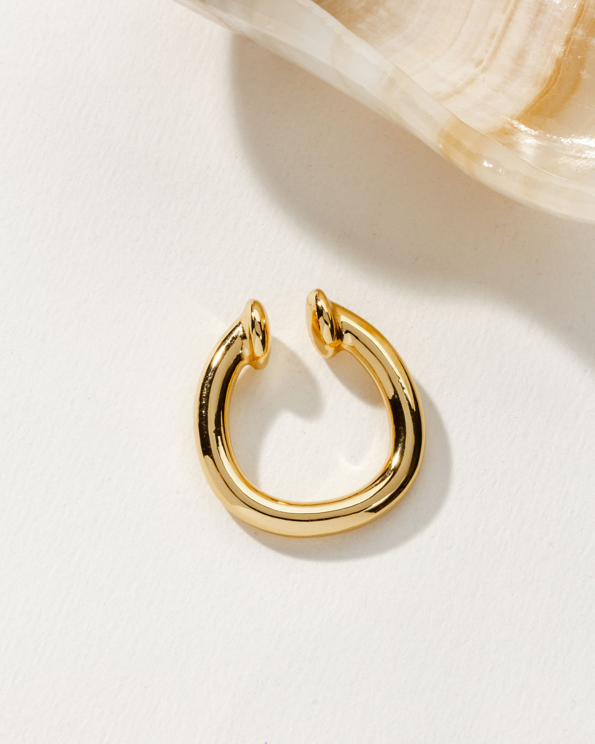 High-polish gold Illusive Conch Ear Cuff Adornment on a white surface with a shell in the background