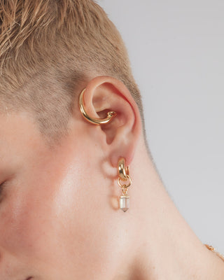 Close-up of a person wearing gold hoop earrings with mystic quarts point charm and gold ear cuff