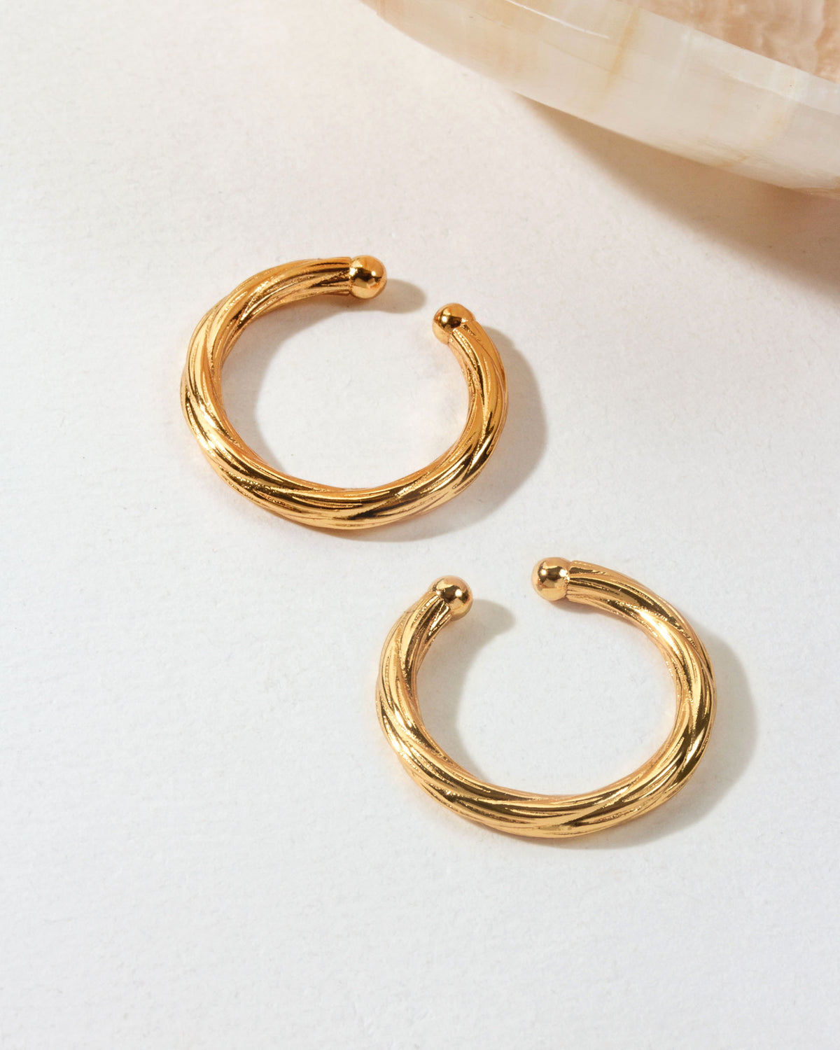 Two gold Helix Twisted Conch ear cuffs are displayed on a white surface.
