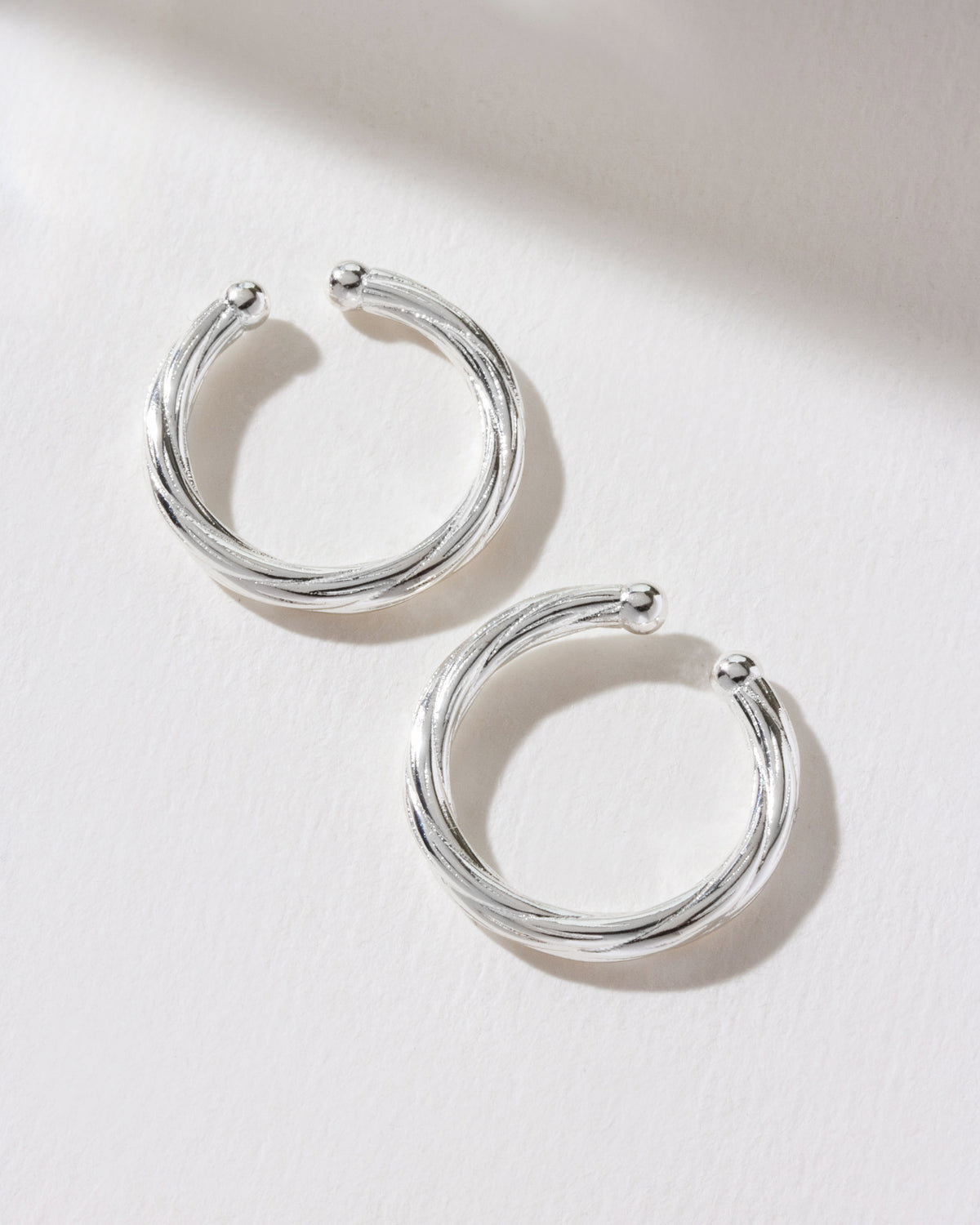 The image shows a pair of silver Helix Twisted Conch ear cuffs.