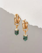 Gold earrings with green gemstones on a light gray background