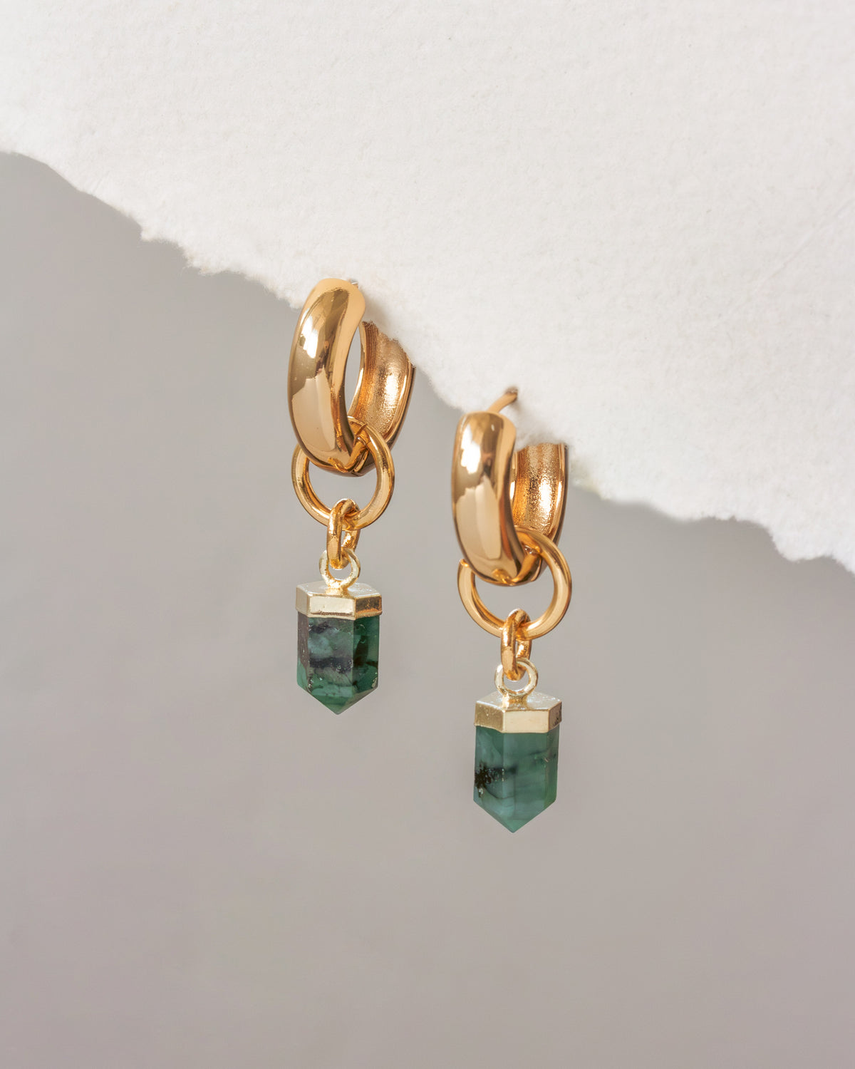 Gold earrings with green gemstones on a light gray background