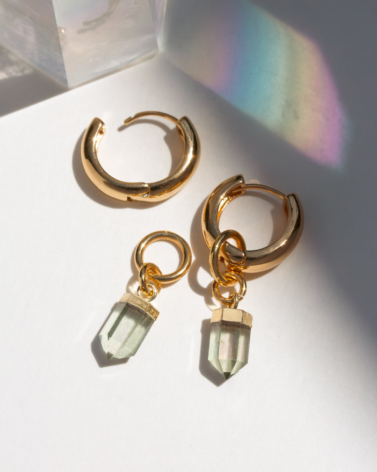 Gold hoop earrings with mystic quartz crystal charms on a white surface