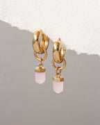 Gold hoop earrings with pink gemstones on a gray background
