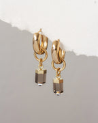 Gold hoop earrings with smoky crystal drops on a light gray background