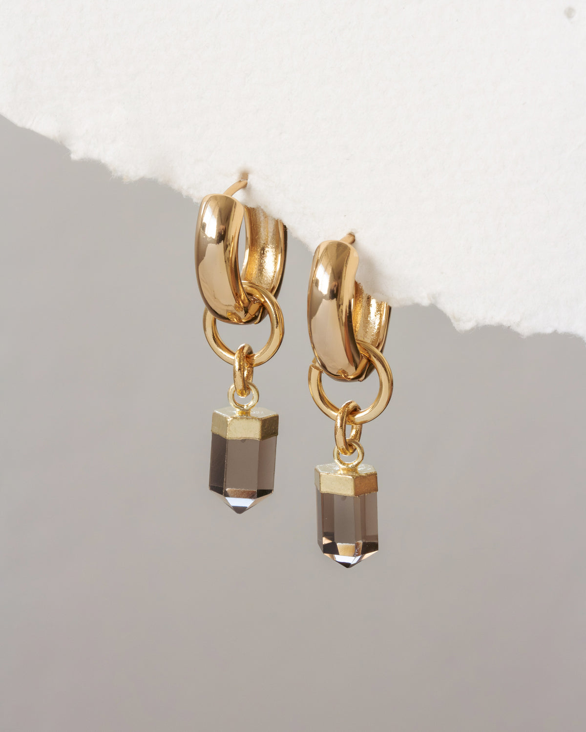 Gold hoop earrings with smoky crystal drops on a light gray background
