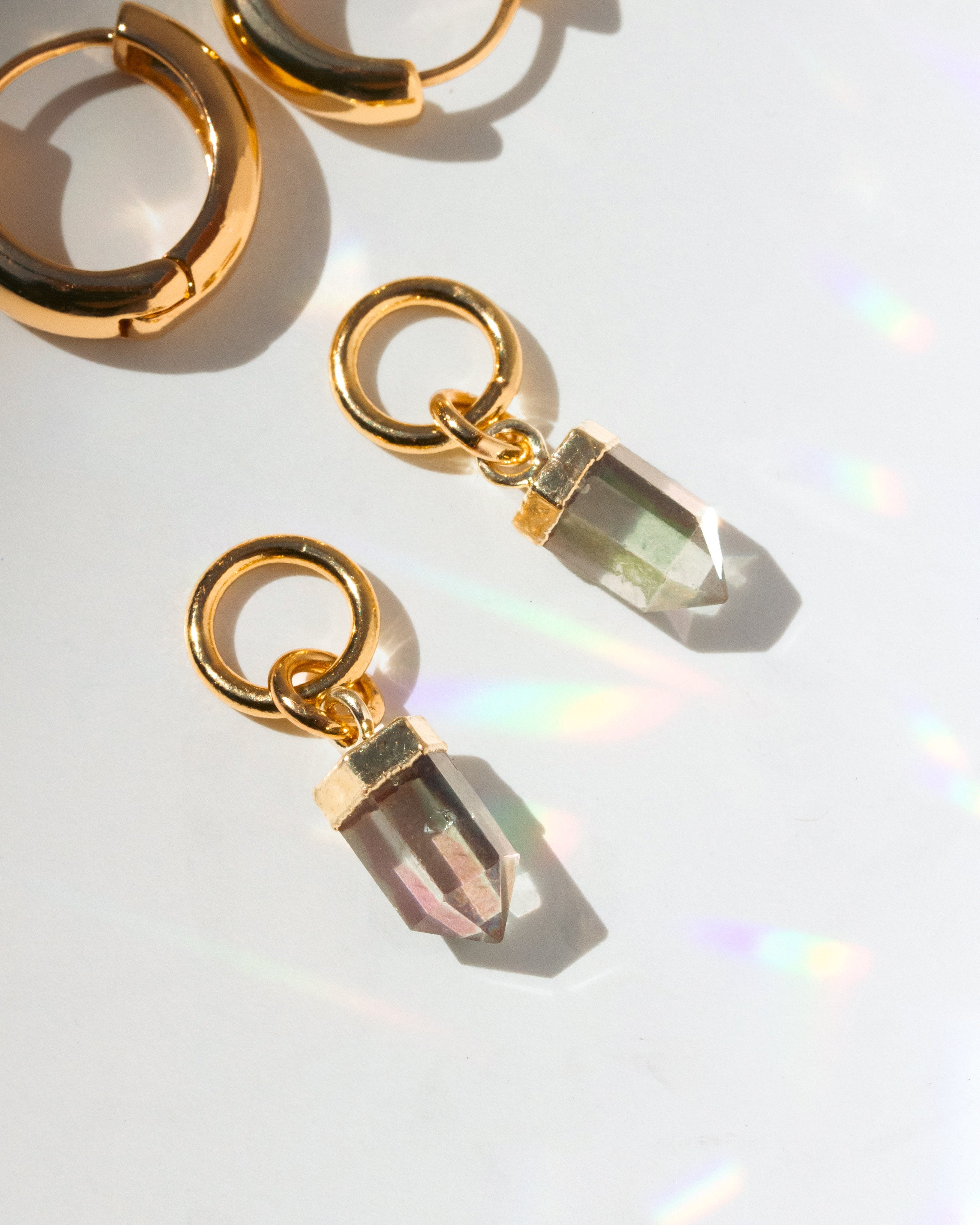 Gold hoop earrings with clear rainbow gemstone drops on a reflective surface