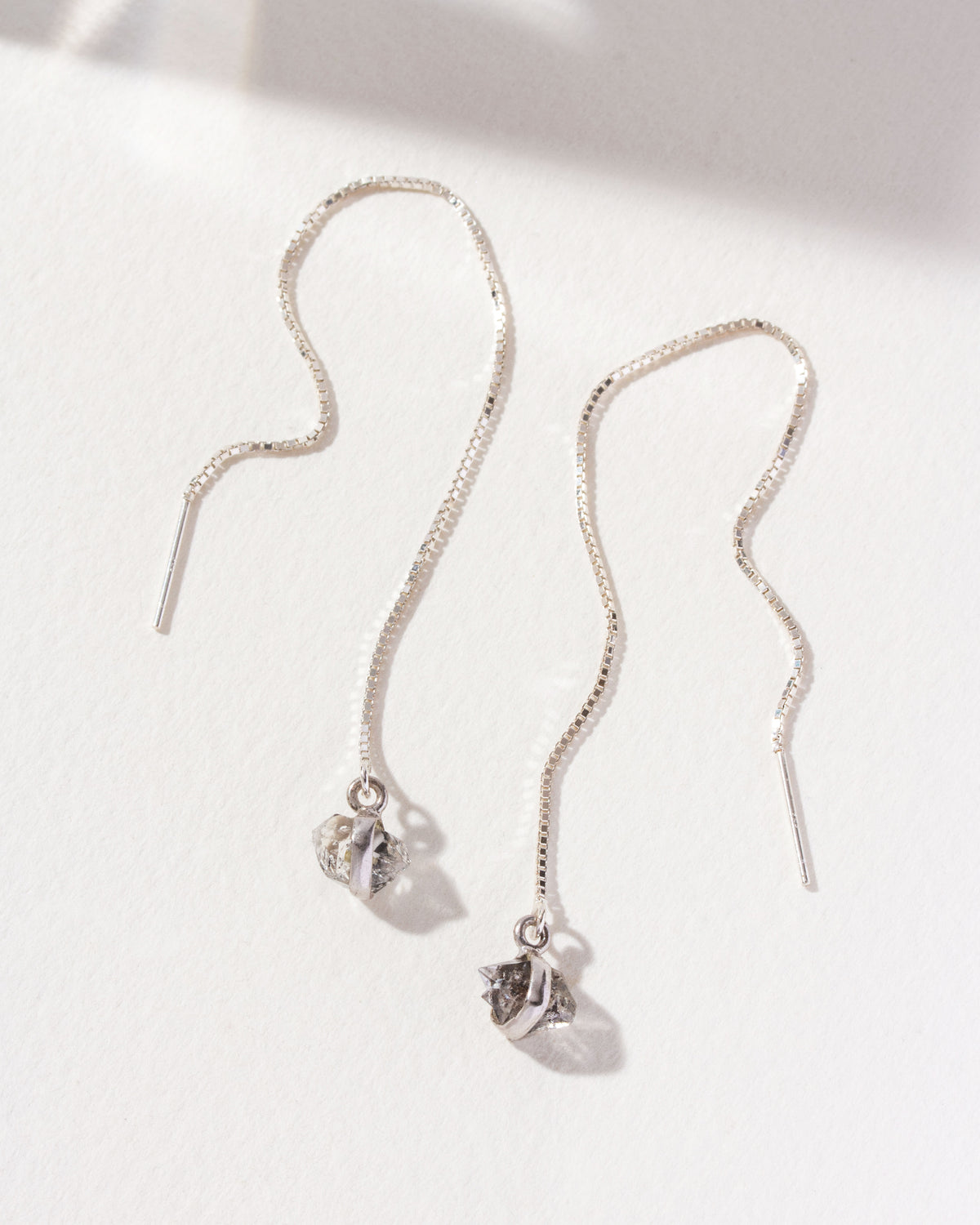 Sterling silver threader earrings featuring Herkimer Quartz stones dangle on a white surface.