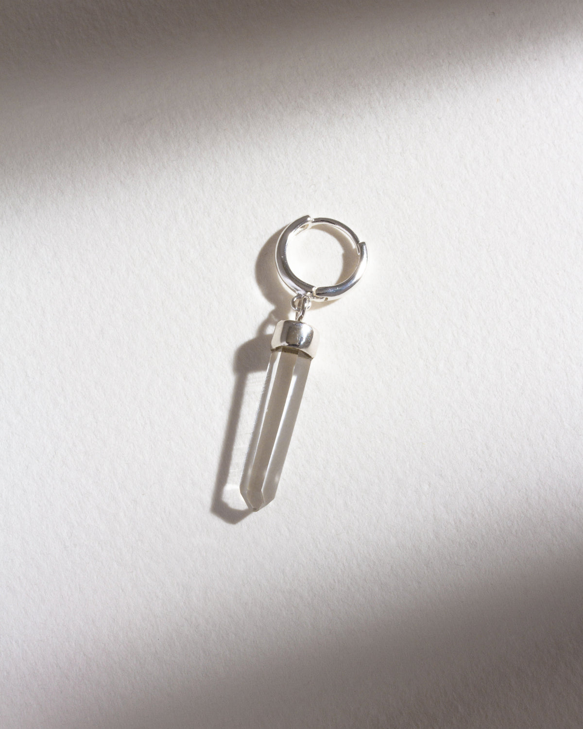 Sterling silver hoop earring with a clear quartz charm, isolated on a white background.