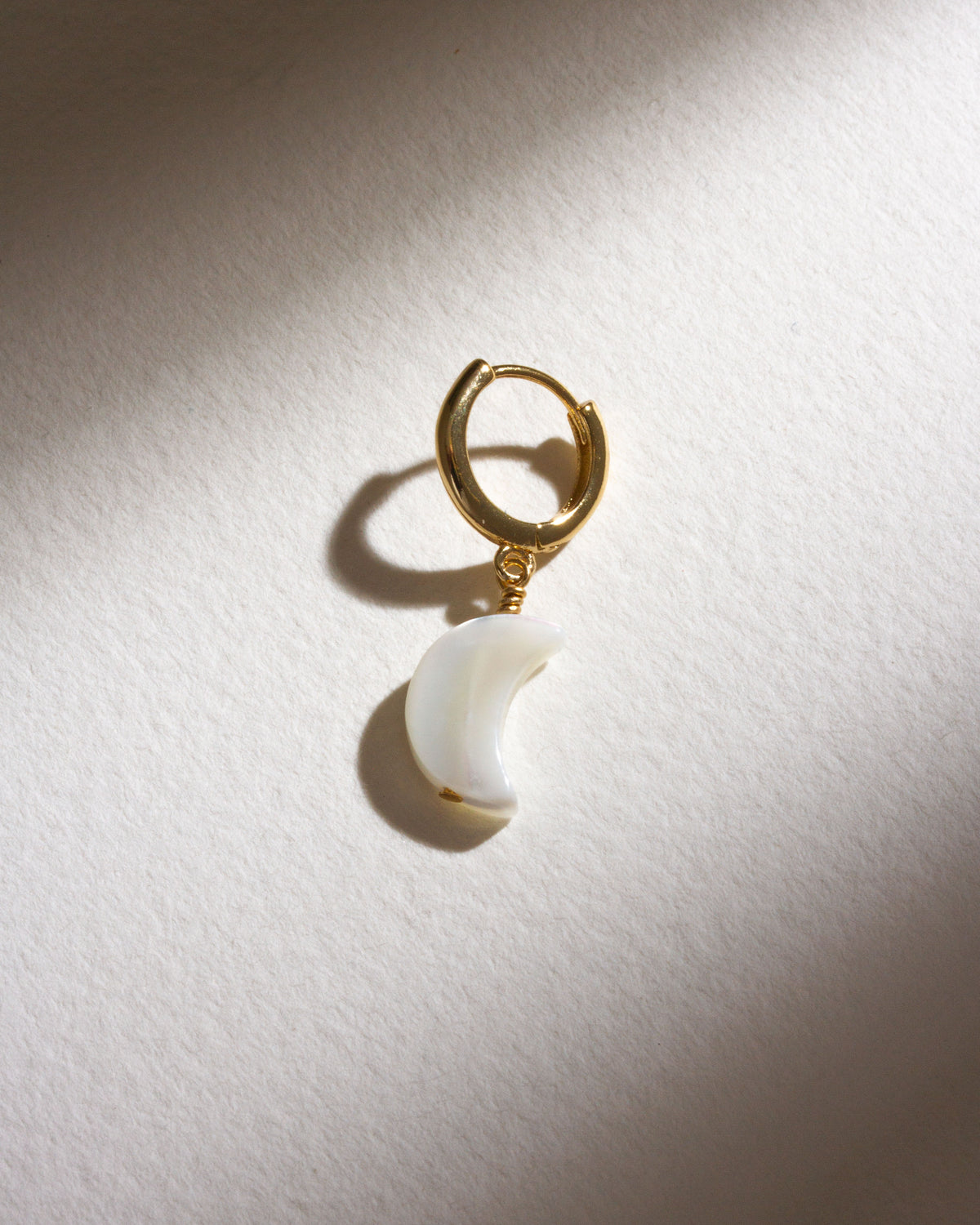Gold hoop earring with a mother of pearl crescent moon charm.