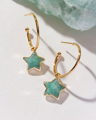Gold hoop earrings with star-shaped green stones on a light background