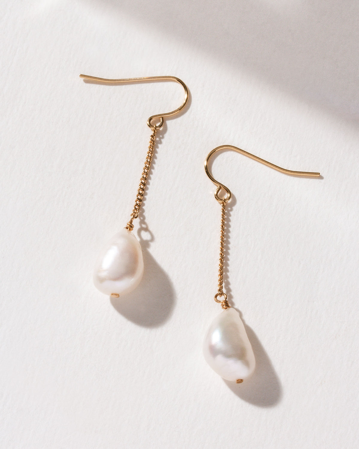 Two Ocean Sway Pearl Drop Earrings with gold chain on a white background.