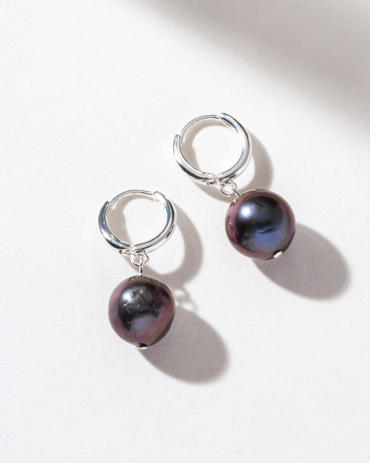 Sterling silver huggie hoop earrings with deep blue freshwater pearls are displayed.