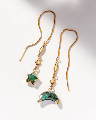 Emerald gemstone gold threader earrings one with star charm and the other with moon charm on a white background.