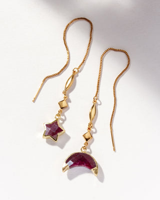 Ruby gemstone gold threader earrings one with star charm and the other with moon charm on a white background.