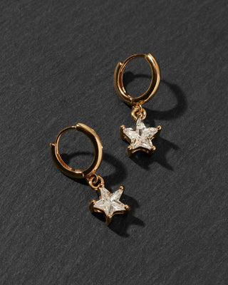 A pair of gold huggie hoop earrings with dangling star-shaped clear cubic zirconia charms.