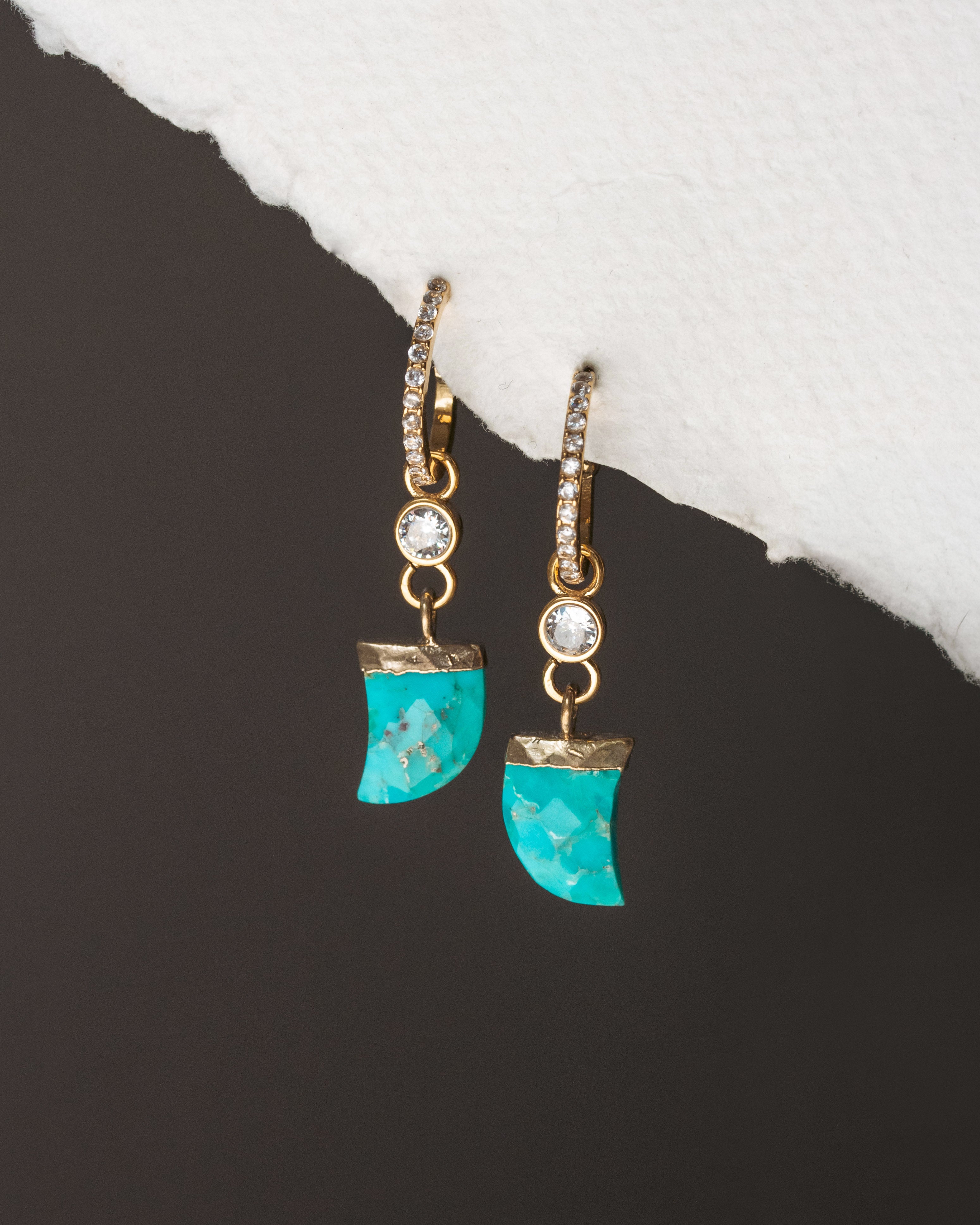 Turquoise earrings with gold accents on a dark surface