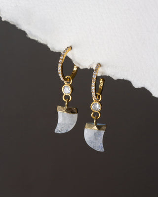 Gold and moonstone earrings on a dark surface with white stone