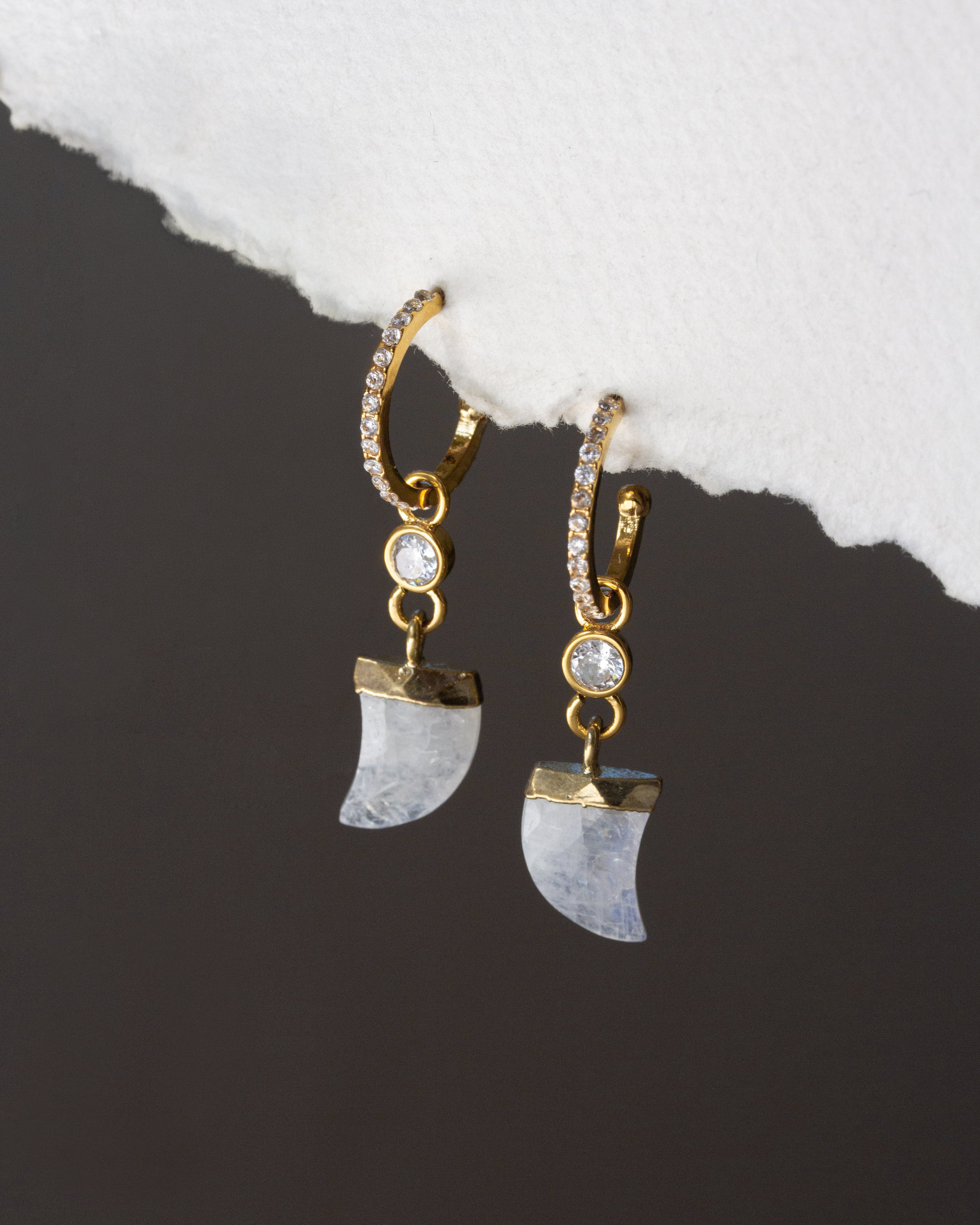 Gold and moonstone earrings on a dark surface with white stone