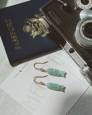 Vintage camera, passport, and fish charm earrings on a textured surface