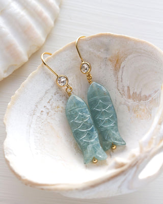 Green fish-shaped earrings with gold hooks and CZ element on a shell background
