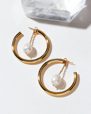 Gold hoop earrings with pearl drops on a light background