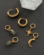 Gold hoop earrings with charms on a dark surface