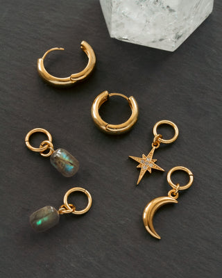 Gold hoop earrings with charms on a dark surface