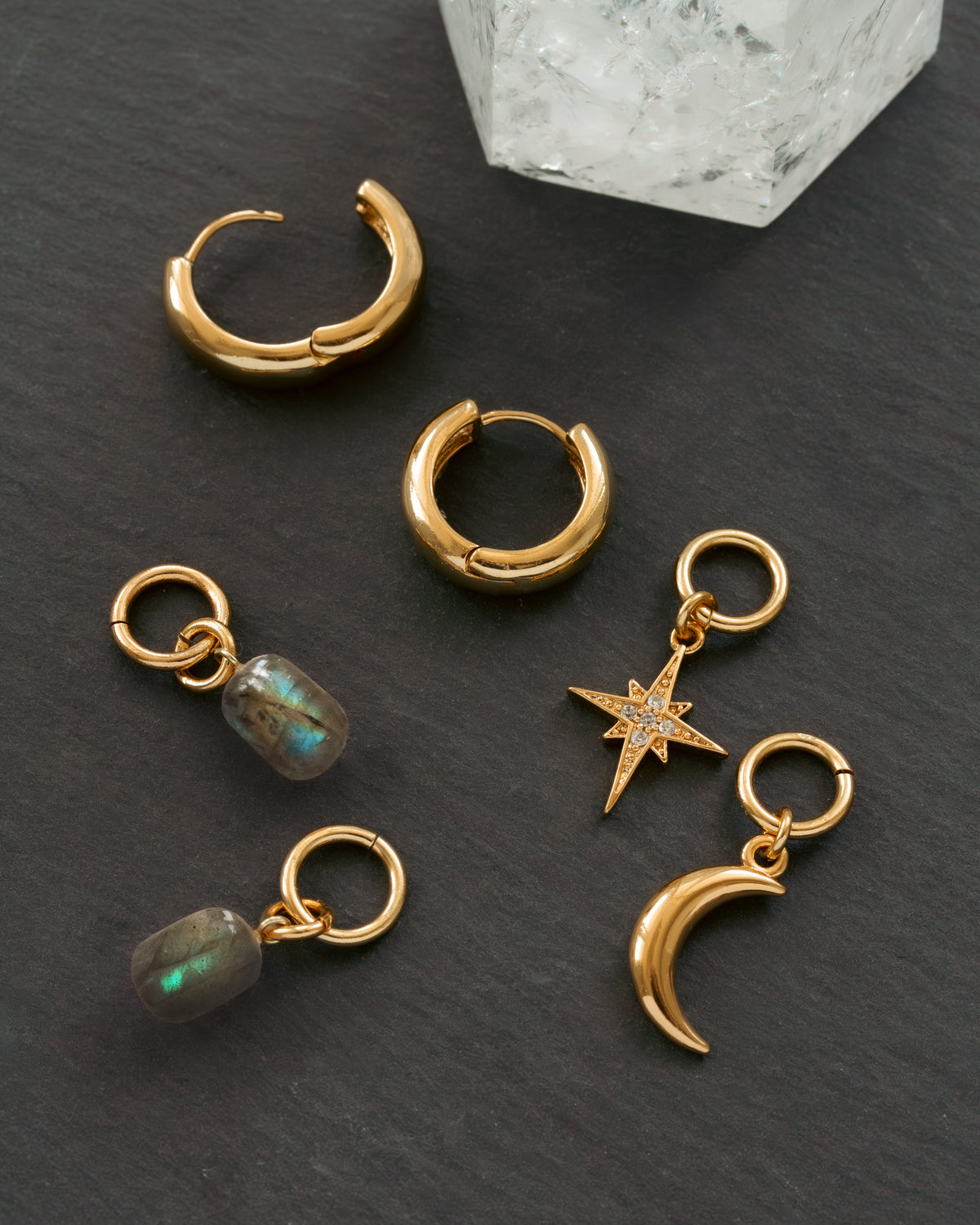Gold hoop earrings with charms on a dark surface