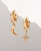 Gold hoop earrings with moon and star charms on a light gray background