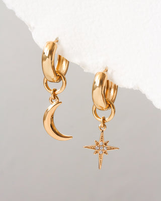 Gold hoop earrings with moon and star charms on a light gray background