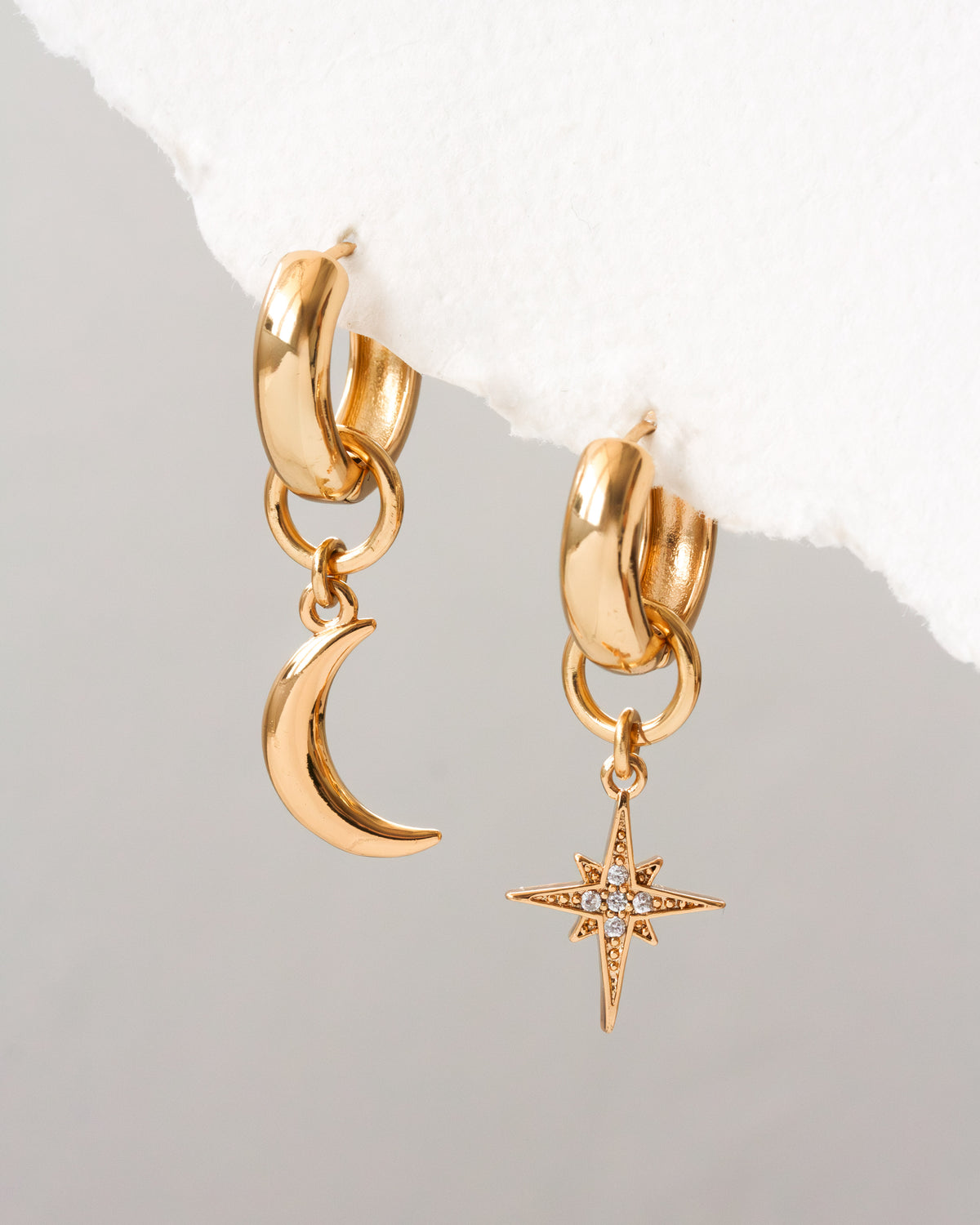 Gold hoop earrings with moon and star charms on a light gray background