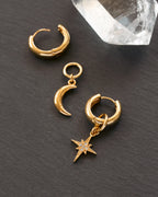 Gold hoop earrings with moon and star charms on a dark surface.