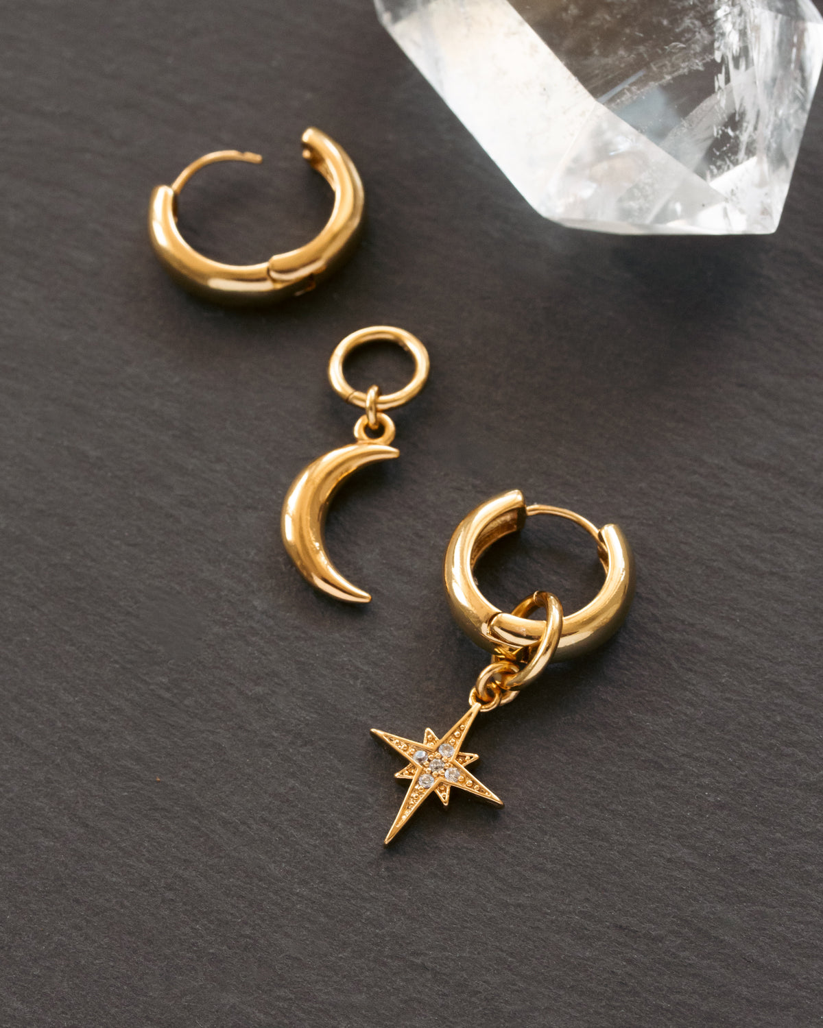 Gold hoop earrings with moon and star charms on a dark surface.