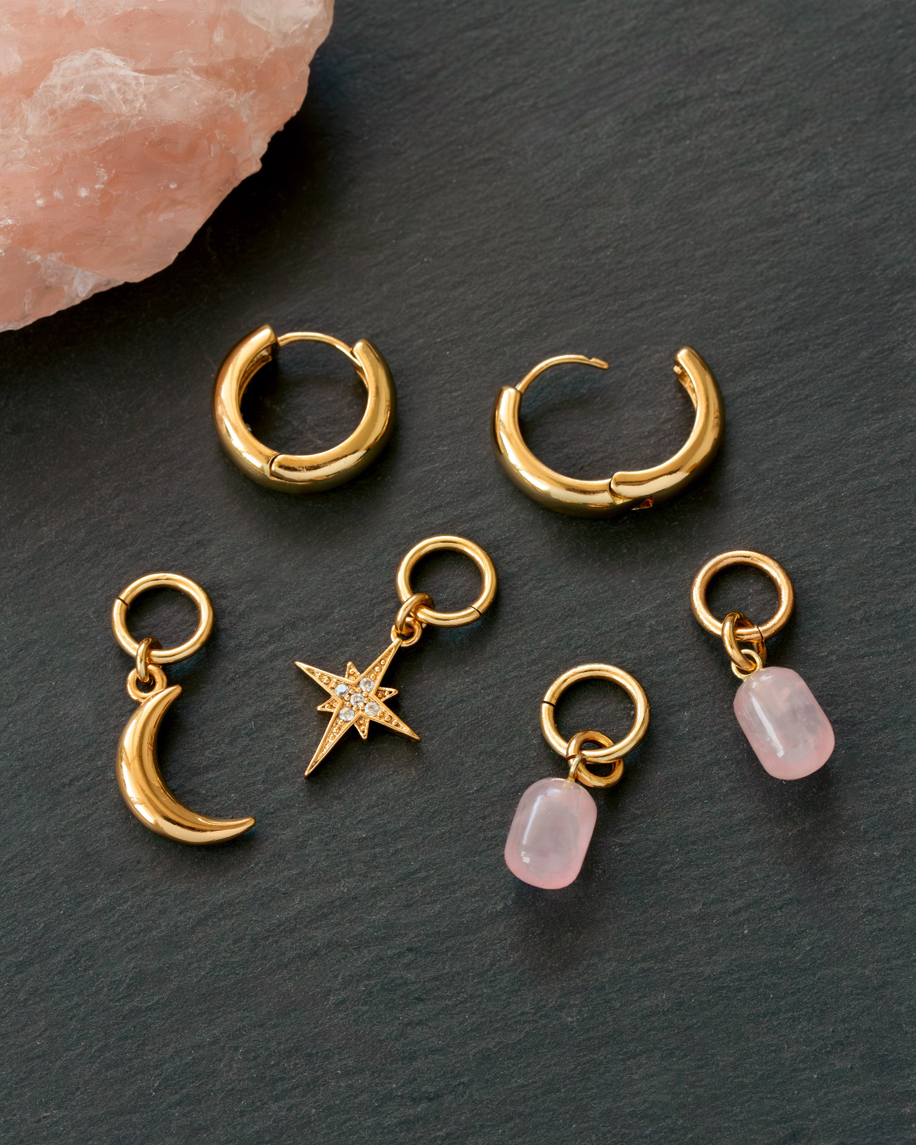 Gold hoop earrings with charms on a dark surface